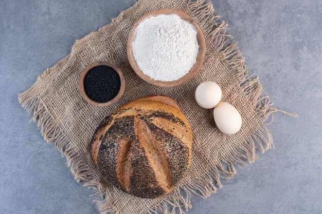 Black sesame seeds, flour, eggs and a sesame coated bread loaf on marble background. High quality photo