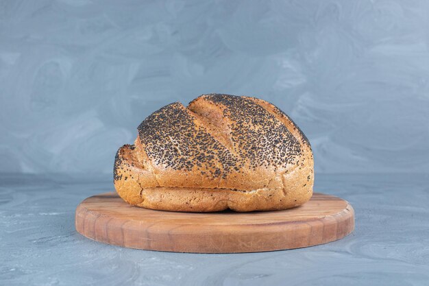 Black sesame seeds on a load of bread of a wooden board on marble background. 