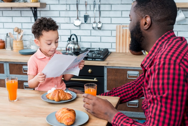 Black son reading greeting card while having breakfast with father