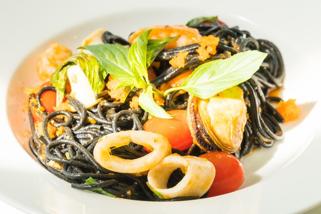 Черные спагетти с морепродуктами в белой тарелке