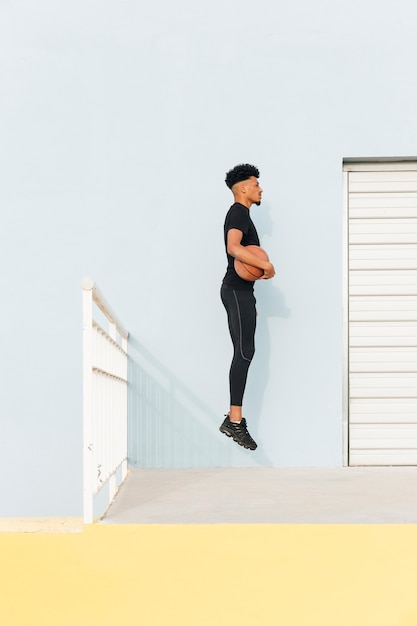 黒のスポーツマンがポーチでバスケットボールでジャンプ
