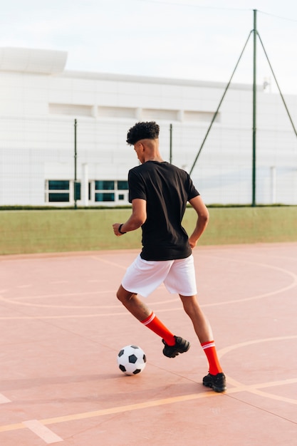 Черный спортсмен играет в футбол на спортивной площадке
