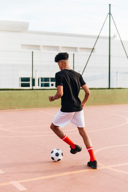 スポーツグラウンドでサッカーと遊ぶ黒いスポーツマン