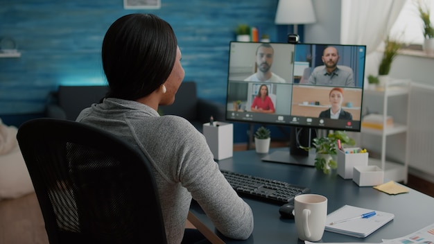 Black student discussing marketing academic ideas with college team having virtual teleconference meeting sitting at desk in living room