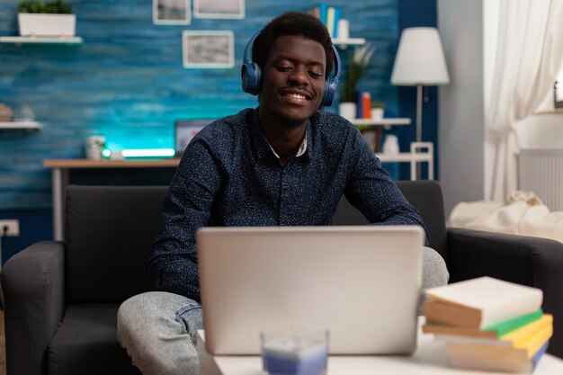 Черный студент в наушниках с аудио-бизнес-курсом на ноутбуке