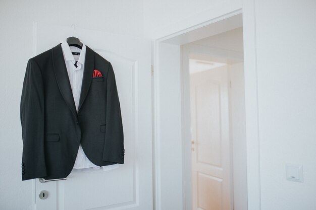 Black suit and a shirt is hanging from a hanger on a door