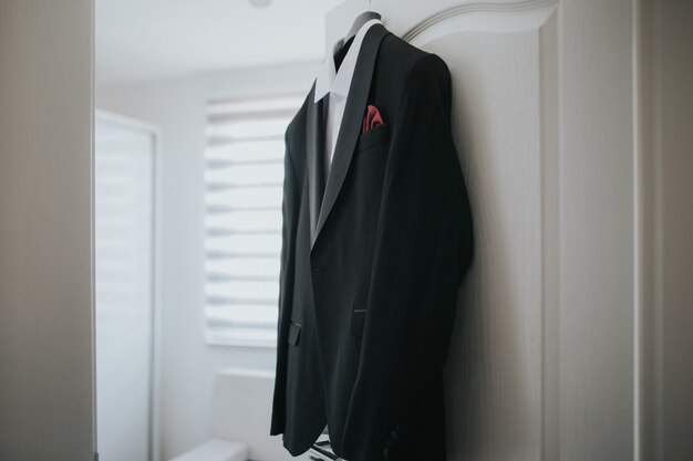 Black suit and a white shirt is hanging from hanger from the door