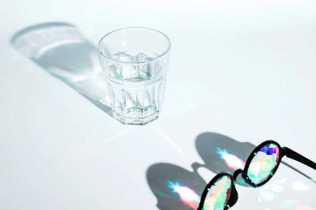 Black sunglasses with multicolor lens and glass of water with shadow on white background