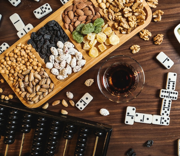 Free photo black tea in armudu glass with various sweets and dominoes on the table