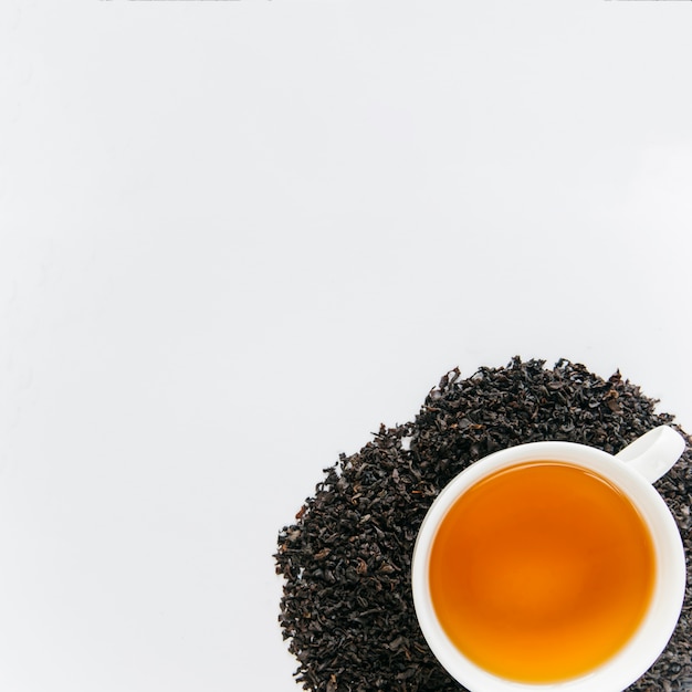 白い背景に分離された乾燥した黒葉の上の紅茶カップ