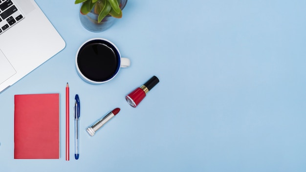 Black tea; laptop; plant; stationery and lipsticks over blue background