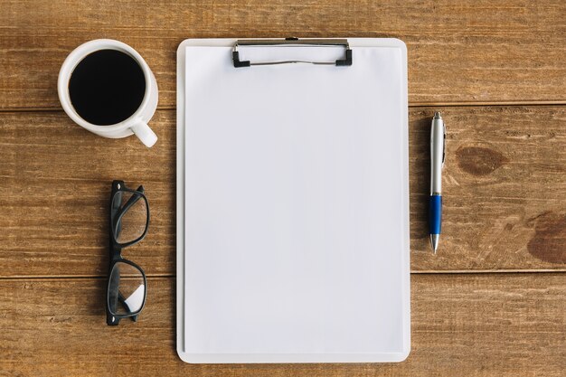 Black tea; pen; spectacles and blank white papers with clipboard on wooden background