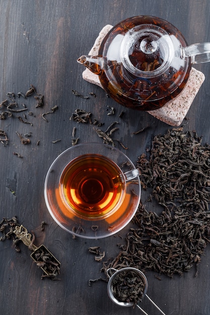 Black tea with dry tea, brick in teapot and cup on wooden surface, top view