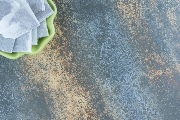 Free photo black teabags in green bowl on marble table.