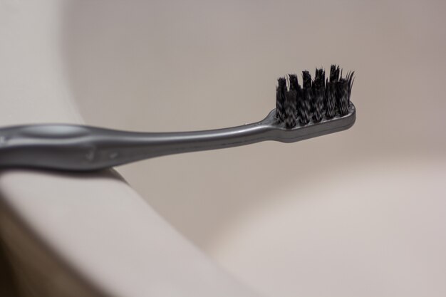 白い背景の後ろのバスルームに置かれた黒い歯ブラシ