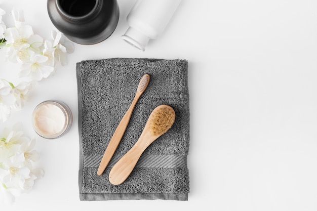 Free photo black towel; brush; moisturizing cream; flowers and container on white background