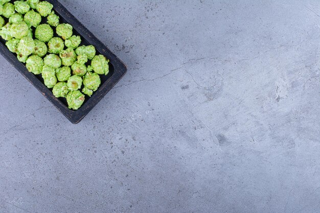 Black tray holding a crunchy pile of candied popcorn on marble surface