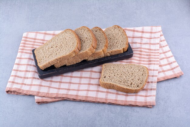 Black tray of sliced brown bread on a folded towel on marble surface