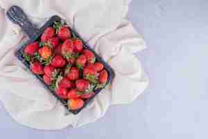 Free photo black tray on white fabric with a pile of strawberries on marble background. high quality photo