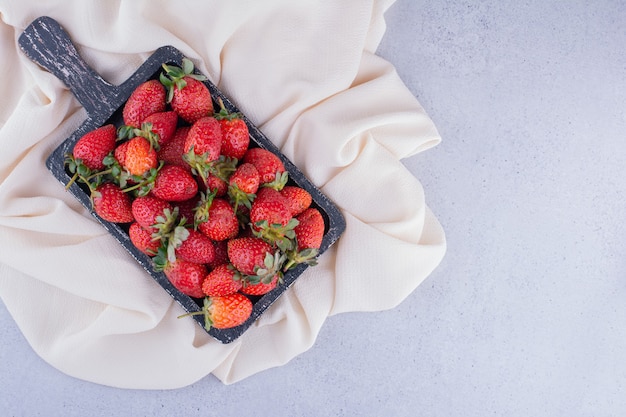 Black tray on white fabric with a pile of strawberries on marble background. High quality photo