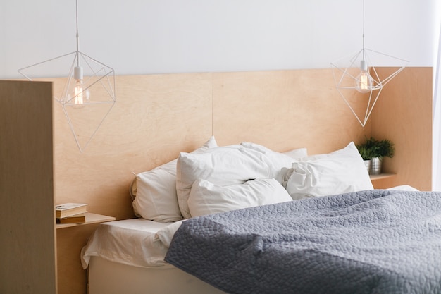 Black and white bed with wooden bedhead in loft interior, geometric lights