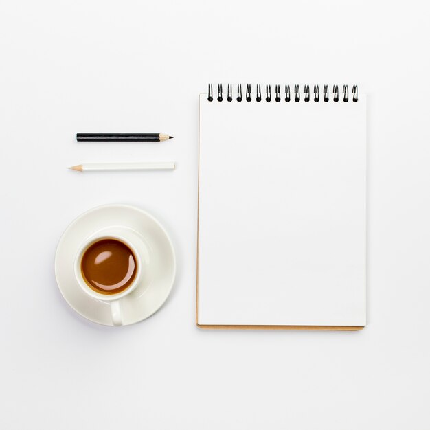 커피 컵과 사무실 책상에 빈 나선형 메모장 검은 색과 흰색 연필