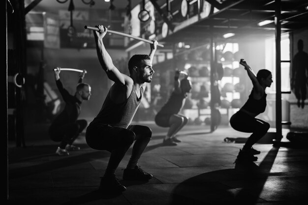 Black and white photo of group of athletes exercising with weight bars on sports training in a gym