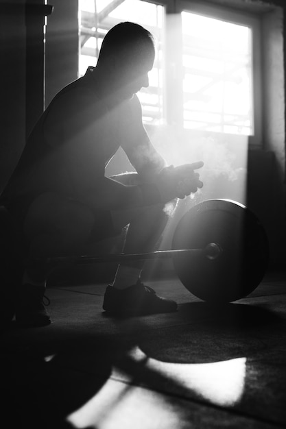 손에 활석 가루를 사용하고 체육관에서 웨이트 트레이닝을 준비하는 스포츠맨의 흑백 사진