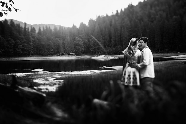 Black and white picture of kissing newlyweds standing in high grass before mountain lake