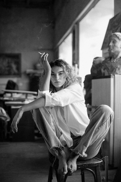 Black and white portrait of beautiful woman posing indoors while smoking a cigarette