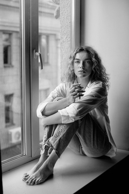 Free photo black and white portrait of beautiful woman posing indoors on a windowsill