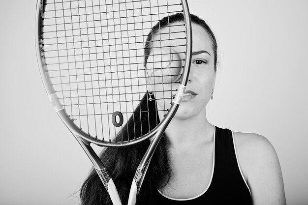 白い背景に立っている間テニスラケットを保持しているスポーツ服を着た美しい若い女性プレーヤーの黒と白の肖像画