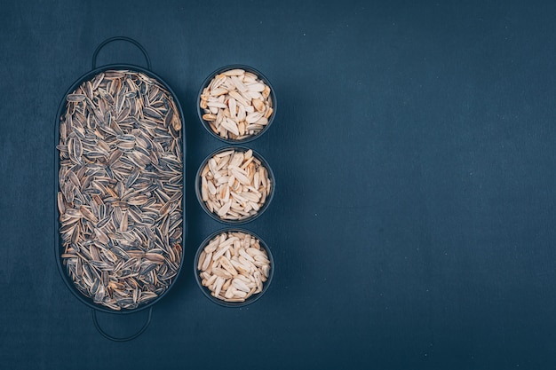 Black and white sunflower seeds in a bowls and plate top view on a black background. space for text