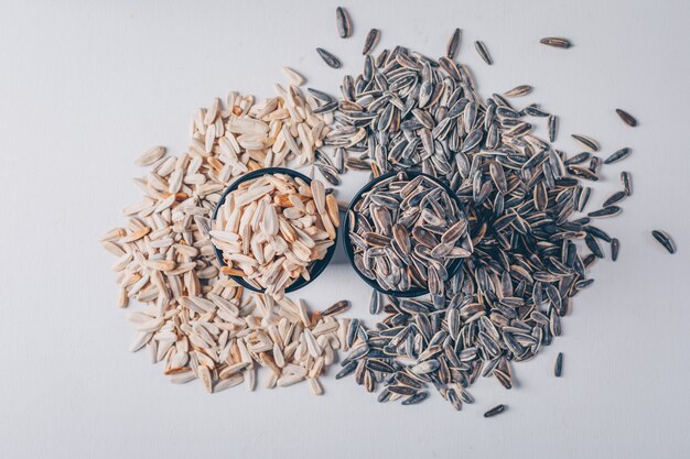 Black and white sunflower seeds in bowls on white background, top view.