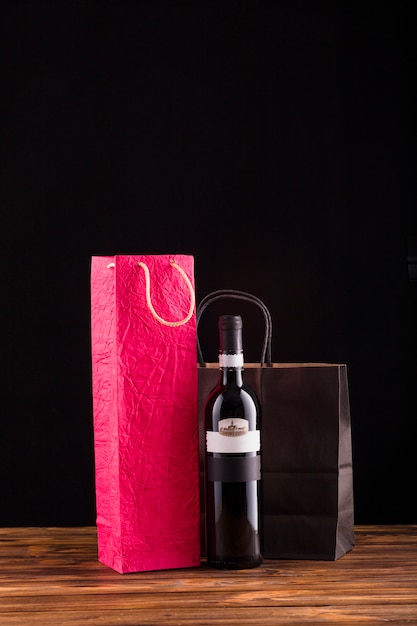 Черная бутылка вина с красивым бумажным пакетом над деревянным столом