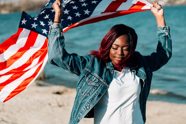 Black woman holding American flag over head closing eyes
