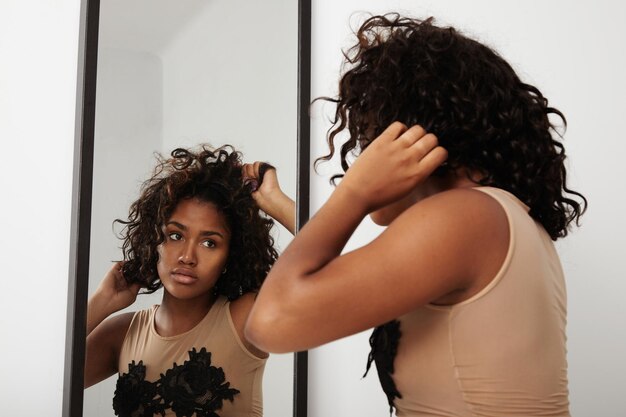 Черная женщина надевает парик, глядя в зеркало