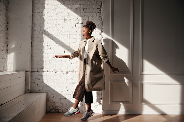 Free photo black woman in trench coat dancing under sunlight