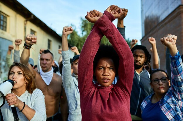 Black woman with clenched fists above her head protesting with group of people on the streets