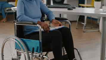 Free photo black woman with disabilities, invalid, disabled paralized handicapped sitting immobilized in wheelchair holding clipboard with financial documents. african manager working in business office room