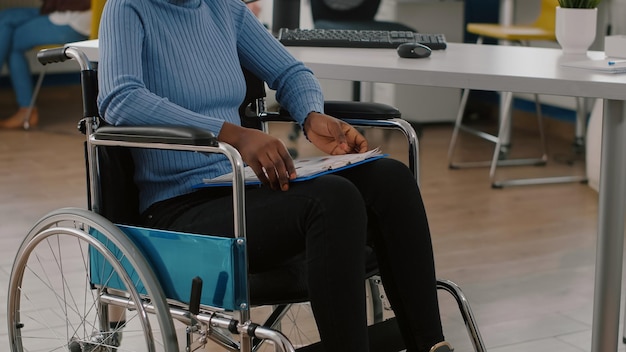 장애가 있는 흑인 여성, 장애인, 장애인 마비 장애인 휠체어에 고정된 재정 문서 클립보드를 들고. 비즈니스 사무실에서 일하는 아프리카 매니저