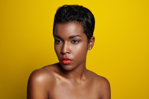 Black woman with a short haircut watching aside bright yellow background