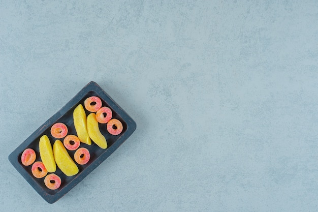 A black wooden board of banana shaped chewing candies with round orange jelly sweets in the shape of rings