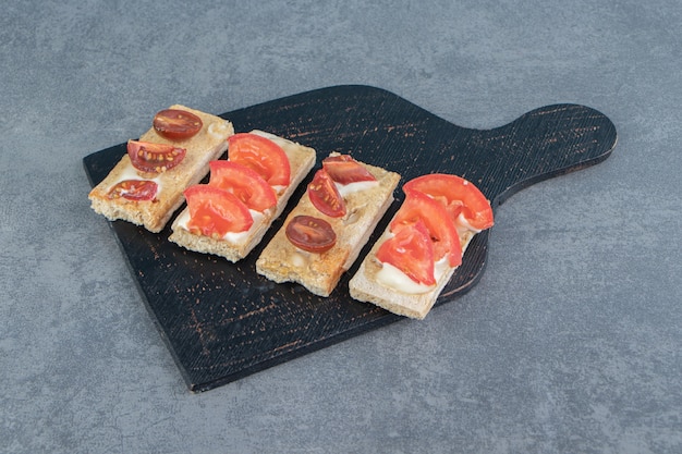 A black wooden board of crispy toasts with tomatoes.