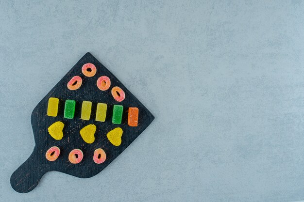 A black wooden board full of colorful fruit jelly candies on a white surface