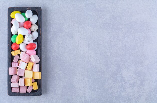 A black wooden board full of sugary colorful candies. High quality photo