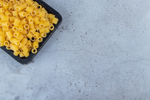 Free photo a black wooden board of raw dry ditali rigati pasta .