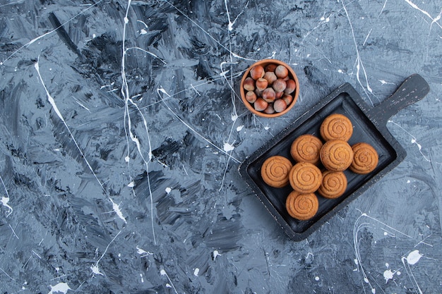 Черная деревянная доска сладкого свежего круглого печенья для чая со здоровыми орехами на мраморном фоне.