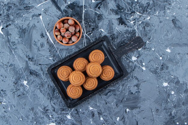 A black wooden board of sweet fresh round cookies for tea with healthy nuts on a marble background . 