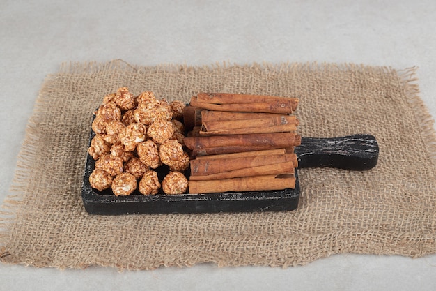 Free photo black wooden tray on a piece of fabric with stacks of popcorn candy and cinnamon cuts on marble.